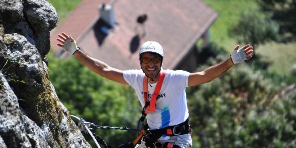 Lachender Mann hängt im Klettergurt hoch oben am Burgfelsen in Riegersburg 
- 
Naturbursch Training Riegersburg - Teamtraining, Kletterkurse, Hochseilgarten